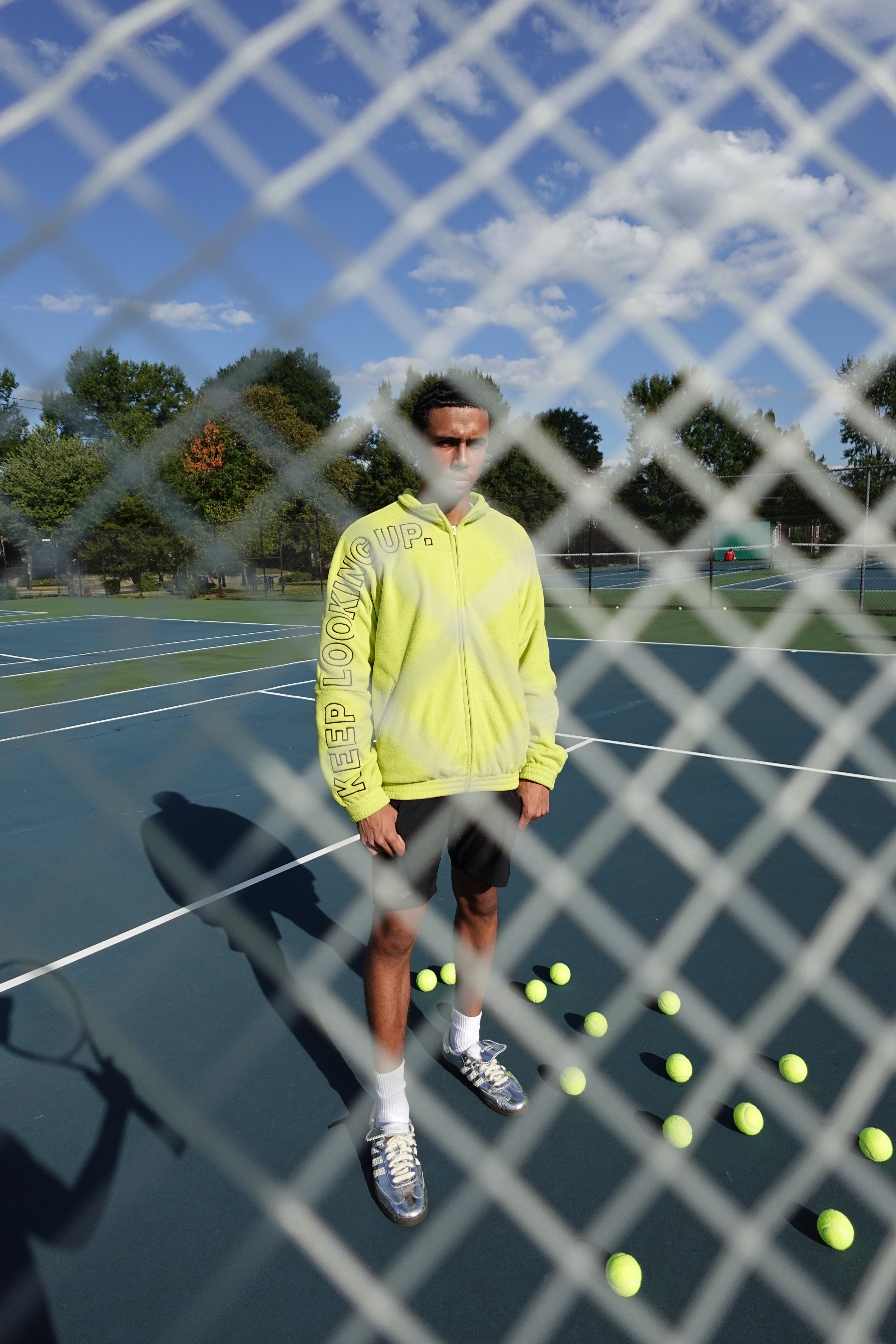 Person in a yellow jacket on a tennis court with tennis balls and rackets.